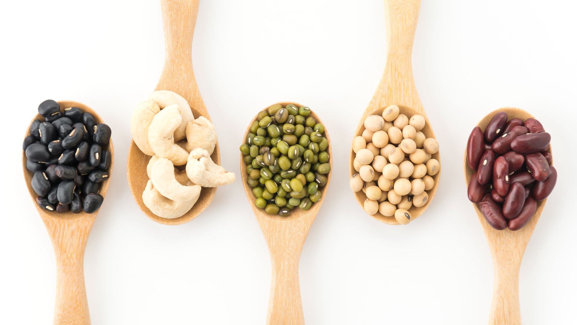 overhead shot of various legumes mixed beans rest on five wooden spoons