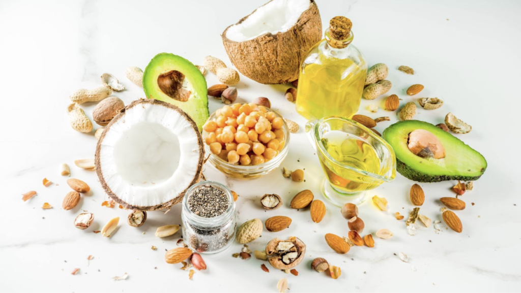 A group of healthy fats, like avocado, coconut, chickpeas, and almonds, are spread out on the table to demonstrate healthy dieting.
